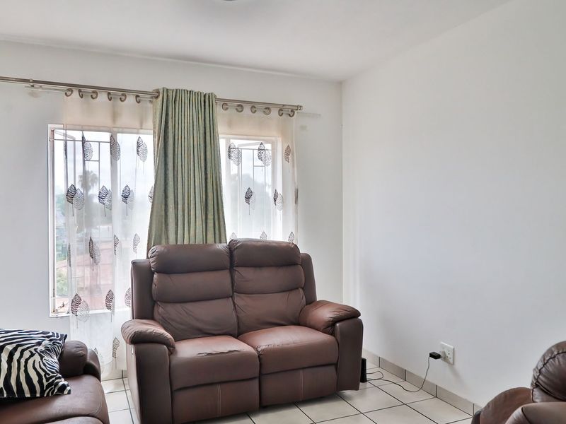 A living room area featuring tiled flooring and a window with security bars, providing a functional and neutral space.