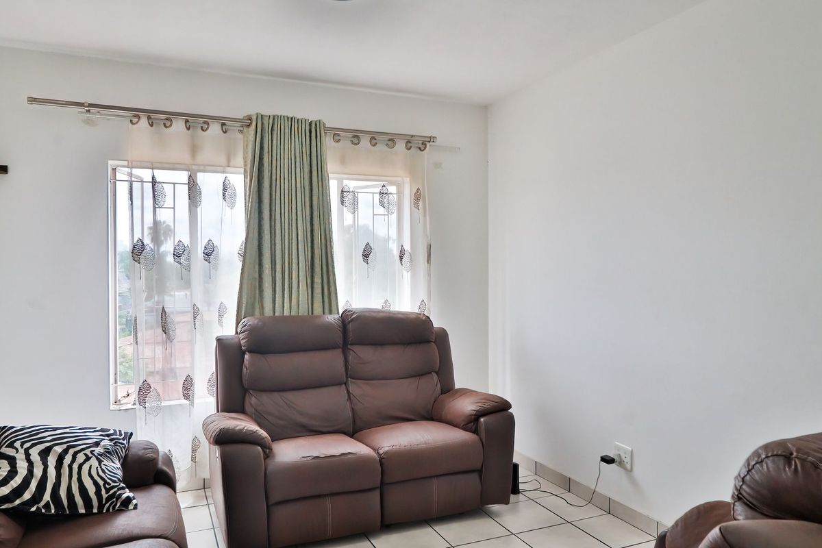 A living room area featuring tiled flooring and a window with security bars, providing a functional and neutral space.