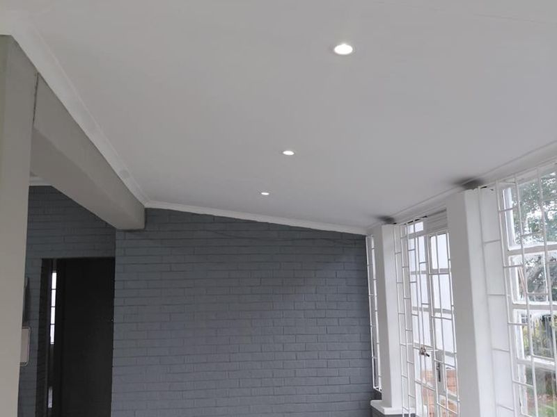 Bright and spacious living area featuring a modern painted brick feature wall, tiled flooring, and recessed downlights with access to the exterior.