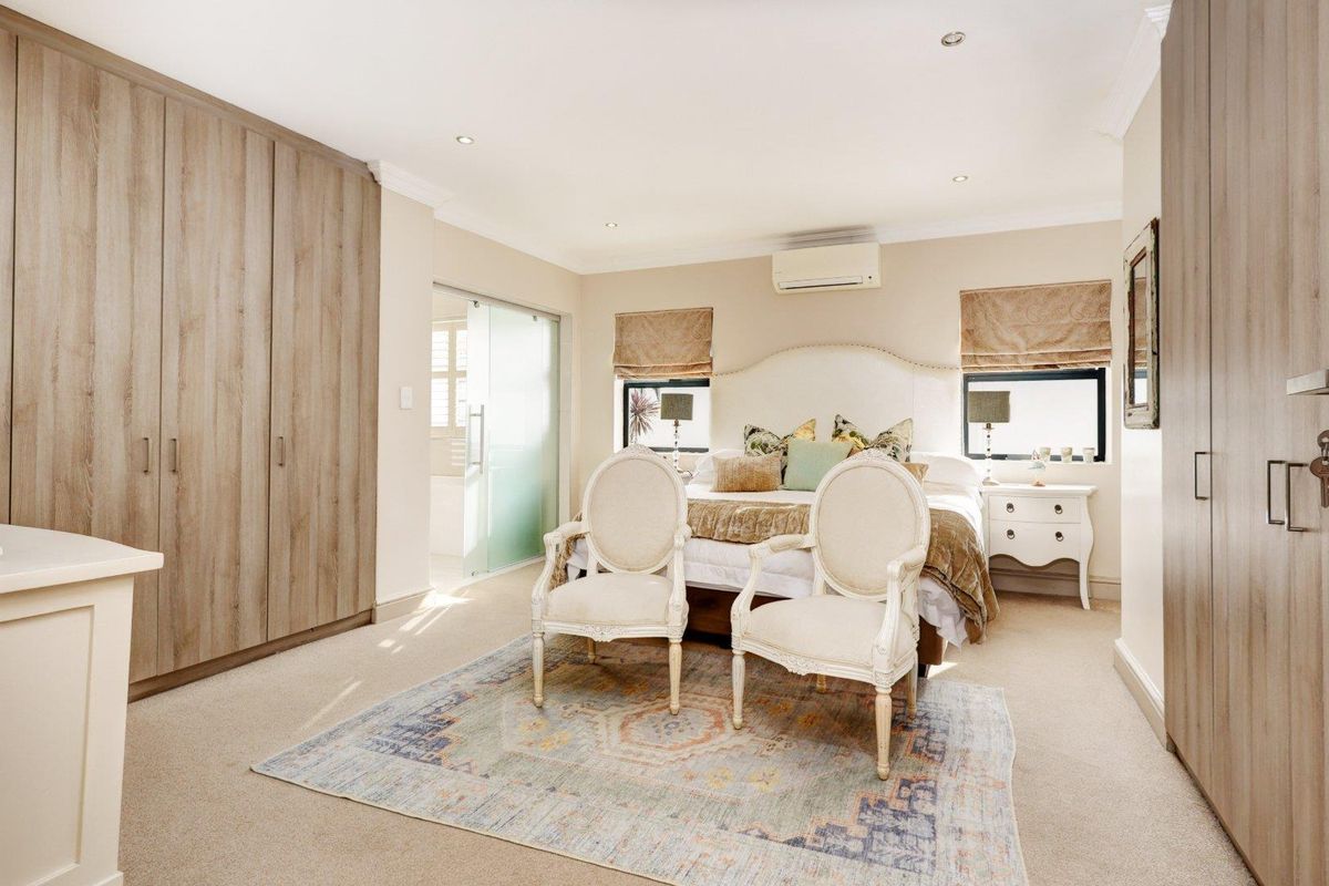 Spacious bedroom featuring extensive built-in cabinetry, recessed downlighting, a wall-mounted air conditioning unit, and an en-suite bathroom with a sliding glass door.