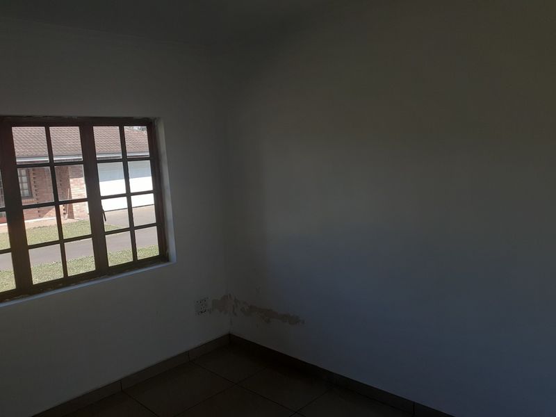 An empty bedroom featuring tiled flooring and a grid-pane window, showing visible signs of wall dampness and paint deterioration requiring maintenance.