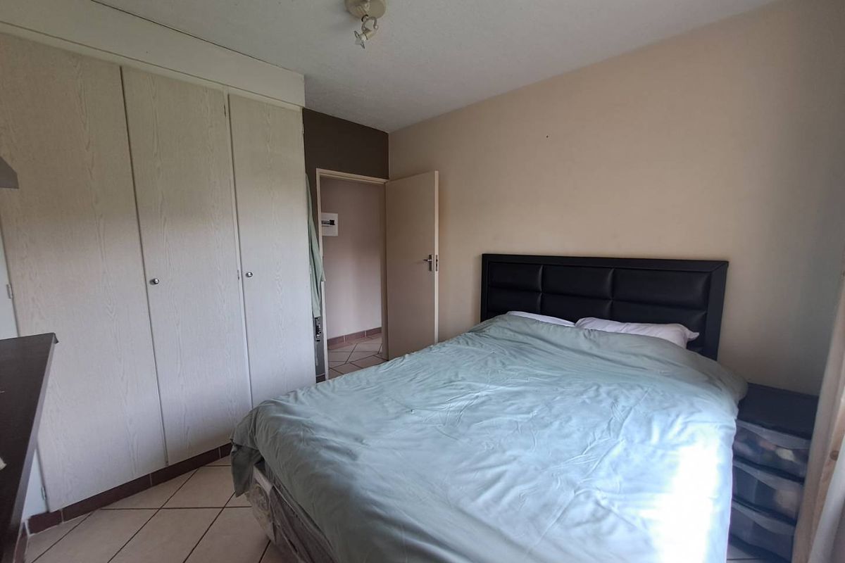 A bedroom featuring built-in wardrobes, tiled flooring, and a neutral color palette, providing a functional space with direct access to the hallway.
