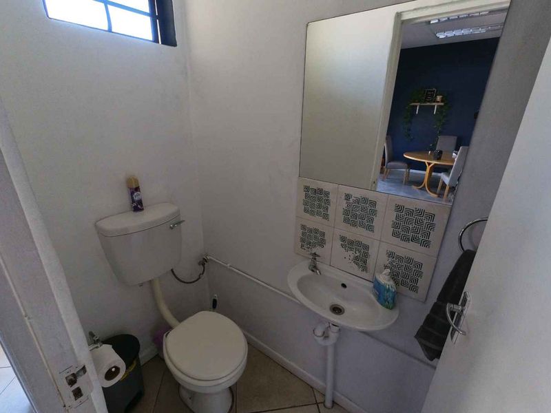 A compact guest bathroom featuring a wall-mounted basin with decorative tiled splashback, a toilet, and a wall-mounted mirror.