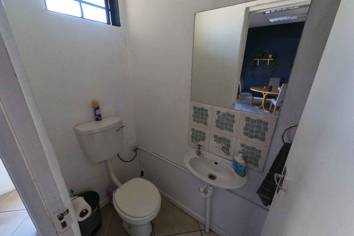 A compact guest bathroom featuring a wall-mounted basin with decorative tiled splashback, a toilet, and a wall-mounted mirror.