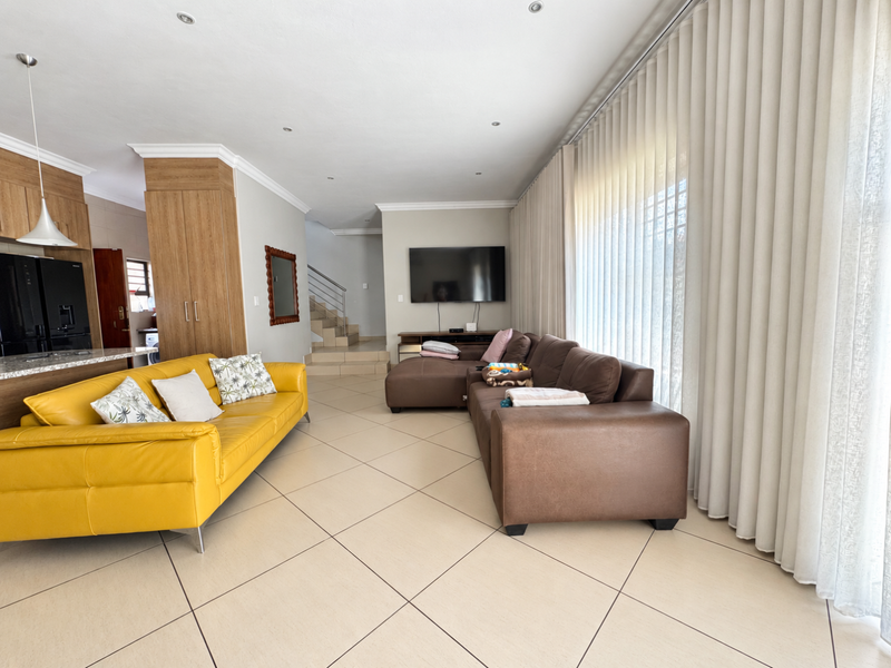 Spacious open-plan living area featuring tiled floors, recessed lighting, and a staircase, seamlessly connecting to the kitchen and dining space.