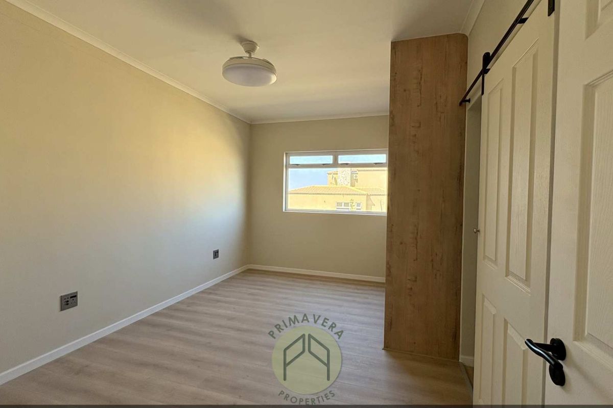 A bright, empty bedroom featuring modern wood-look laminate flooring, a built-in wardrobe with a wood-grain finish, and a sliding barn-style door.