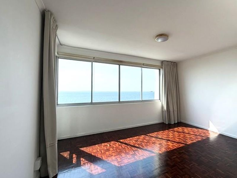 A bright, empty living room featuring classic parquet flooring and a large window offering expansive ocean views.