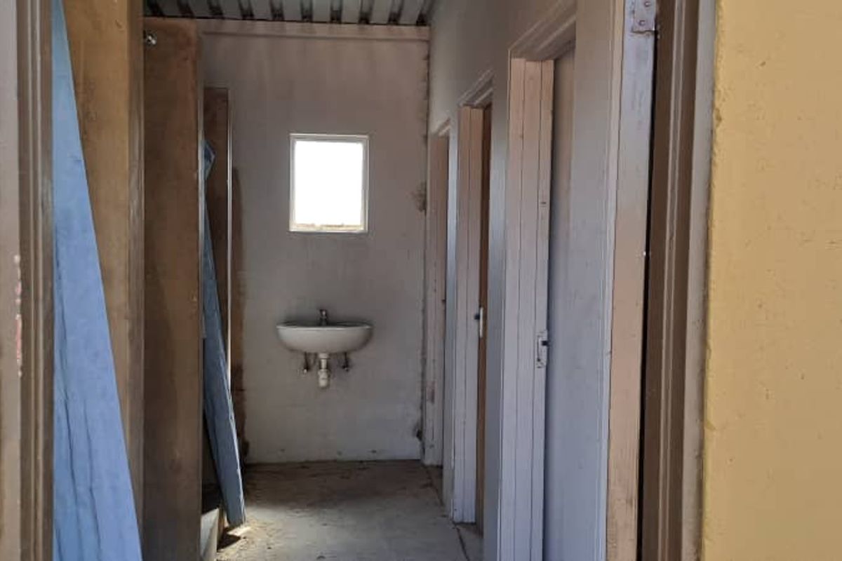 A utilitarian washroom area featuring a wall-mounted basin, multiple door access points, and basic infrastructure, requiring significant renovation and cosmetic updates.
