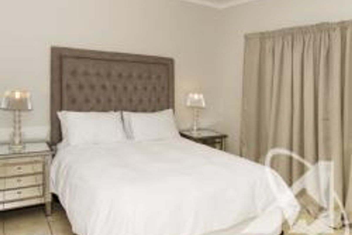 A well-maintained bedroom featuring neutral wall tones, tiled flooring, and floor-to-ceiling curtains.