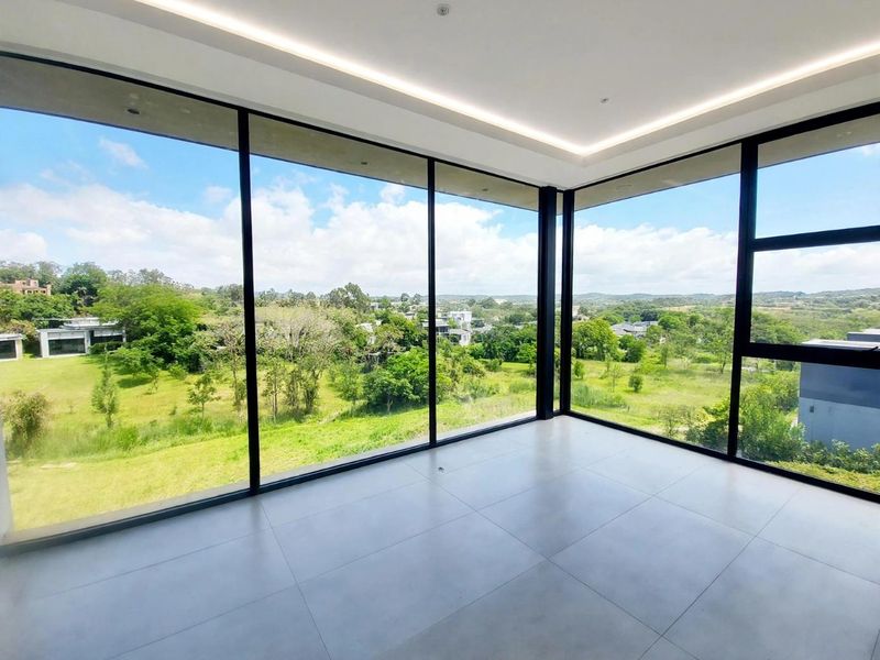 A bright, modern, empty living space featuring expansive floor-to-ceiling windows that offer panoramic views of the surrounding landscape.