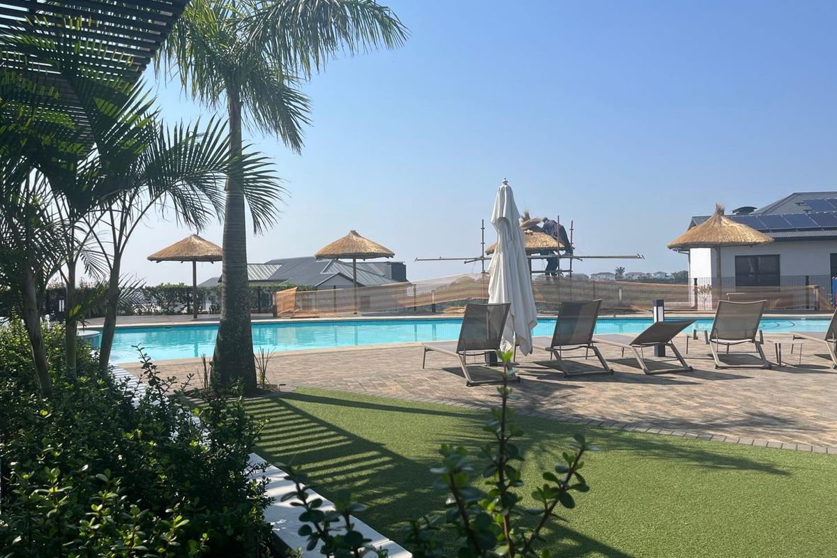Outdoor pool area featuring a paved deck, artificial grass, and thatch umbrellas, currently undergoing maintenance with visible scaffolding.