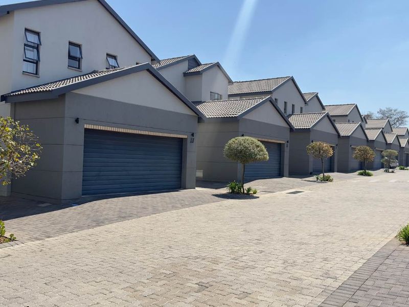 A row of modern townhouse units featuring paved driveways, automated garage doors, and tiled roofing in a well-maintained residential complex.