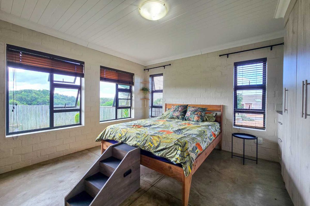 A bright bedroom featuring exposed brick walls, polished concrete flooring, a timber-paneled ceiling, and large windows with fitted blinds.
