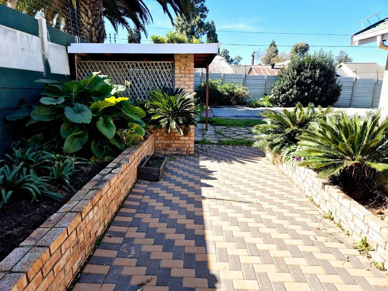 A rear garden area featuring a brick-paved patio, retaining walls, and a covered outdoor structure enclosed by precast boundary walls.