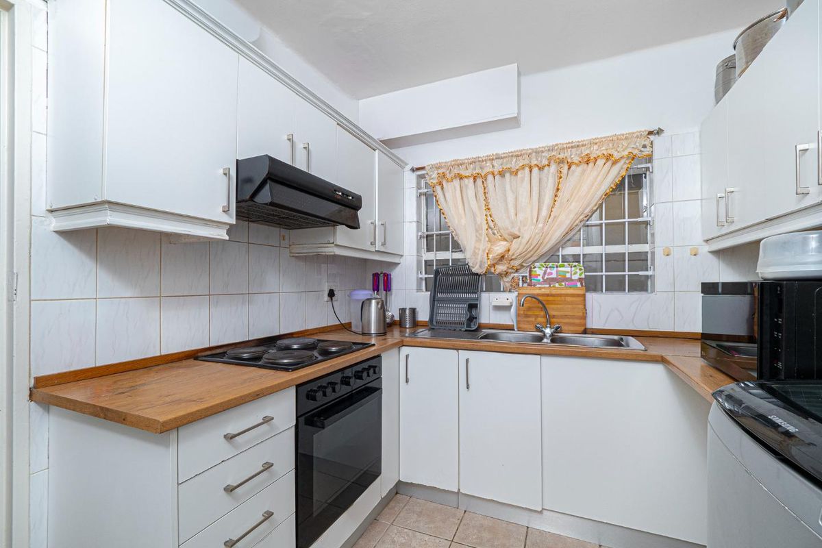 Compact kitchen featuring white cabinetry, wood-look laminate countertops, built-in oven, electric hob, extractor fan, and a stainless steel sink with tiled splashbacks.