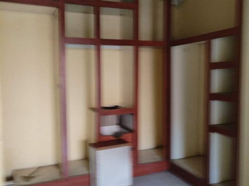 An empty bedroom featuring extensive built-in wooden shelving and tiled flooring, requiring cosmetic updates and ceiling repairs.