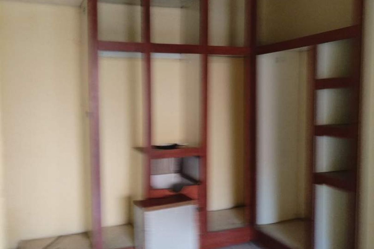 An empty bedroom featuring extensive built-in wooden shelving and tiled flooring, requiring cosmetic updates and ceiling repairs.