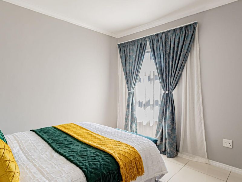 A bright and well-maintained bedroom featuring neutral wall tones, tiled flooring, and classic window treatments.
