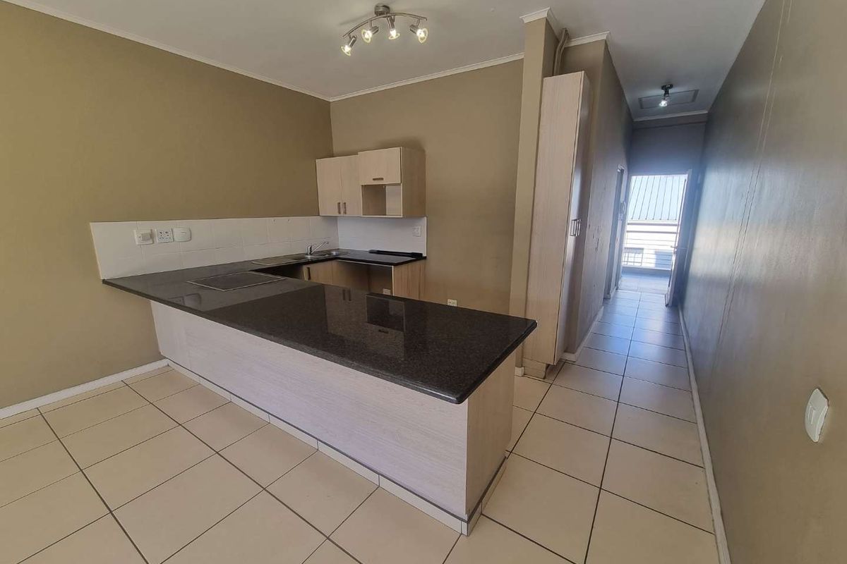 An open-plan kitchen featuring granite countertops, built-in cabinetry, and ceramic floor tiles, leading into a hallway area.