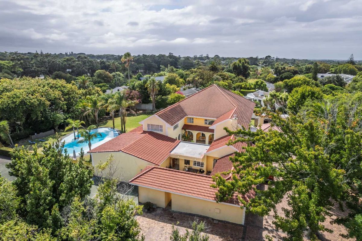 Aerial view of a large residential property featuring a tiled roof, swimming pool, and expansive landscaped garden in a lush neighborhood setting.