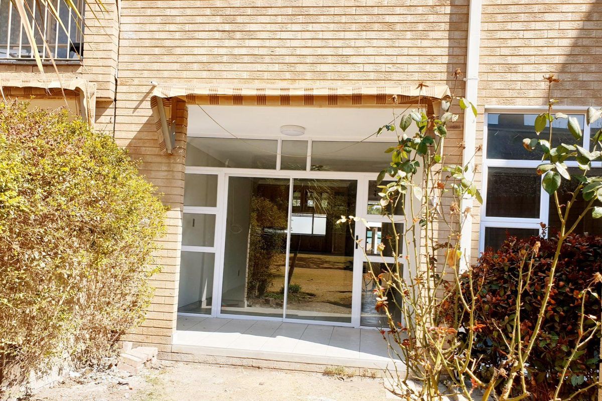 Rear exterior view of an apartment featuring a brick facade, a tiled patio area, and a sliding glass door entrance.