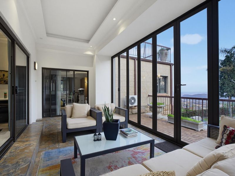 A bright, enclosed patio featuring large glass sliding doors, recessed ceiling lighting, and stone-tiled flooring, offering expansive views and seamless indoor-outdoor flow.