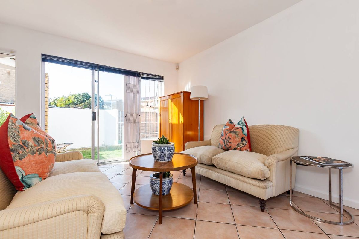 A bright living room featuring tiled flooring and large sliding glass doors that provide direct access to the outdoor garden area.