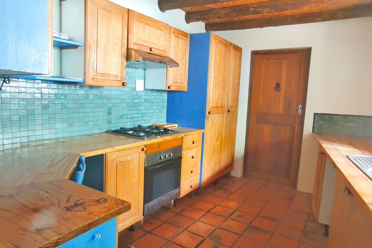 Rustic kitchen featuring wooden cabinetry, tiled backsplash, integrated gas hob and oven, and exposed timber ceiling beams.
