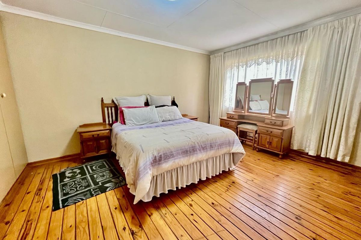 A spacious bedroom featuring polished hardwood flooring, neutral wall finishes, and large windows with installed curtain tracks.
