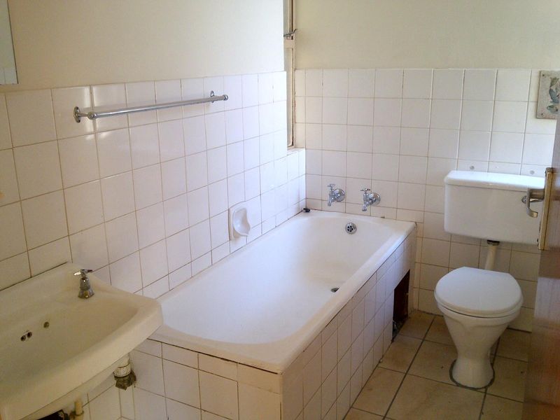 A dated bathroom featuring a standard bathtub, pedestal basin, and toilet with white wall tiling throughout.