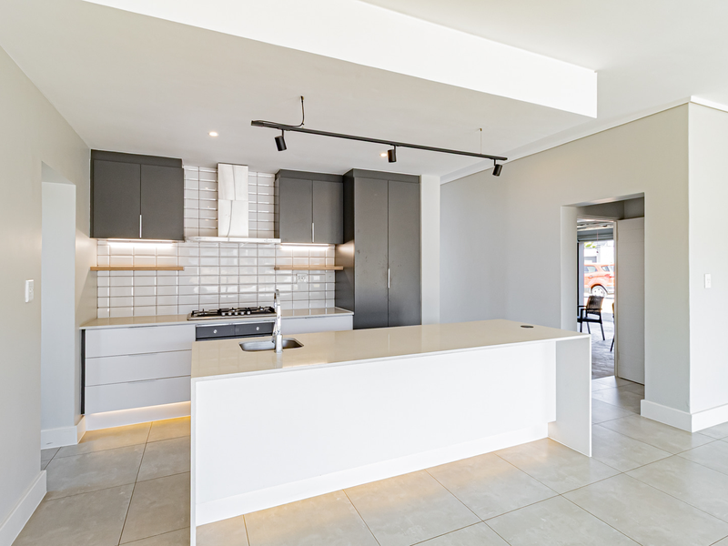 Modern kitchen featuring a central island, sleek grey and white cabinetry, gas hob, extractor fan, and stylish subway tile backsplash with under-cabinet lighting.