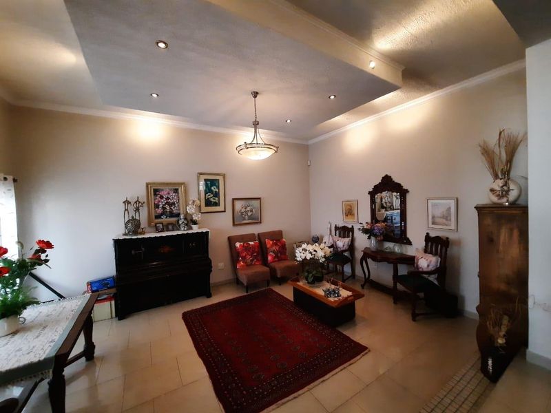 A spacious living room featuring a recessed ceiling with downlights, a central pendant light, and neutral tiled flooring.