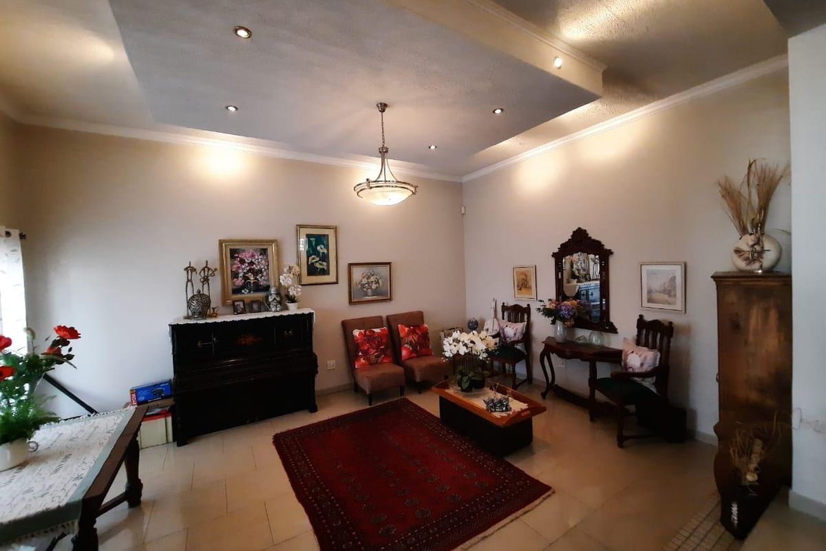 A spacious living room featuring a recessed ceiling with downlights, a central pendant light, and neutral tiled flooring.