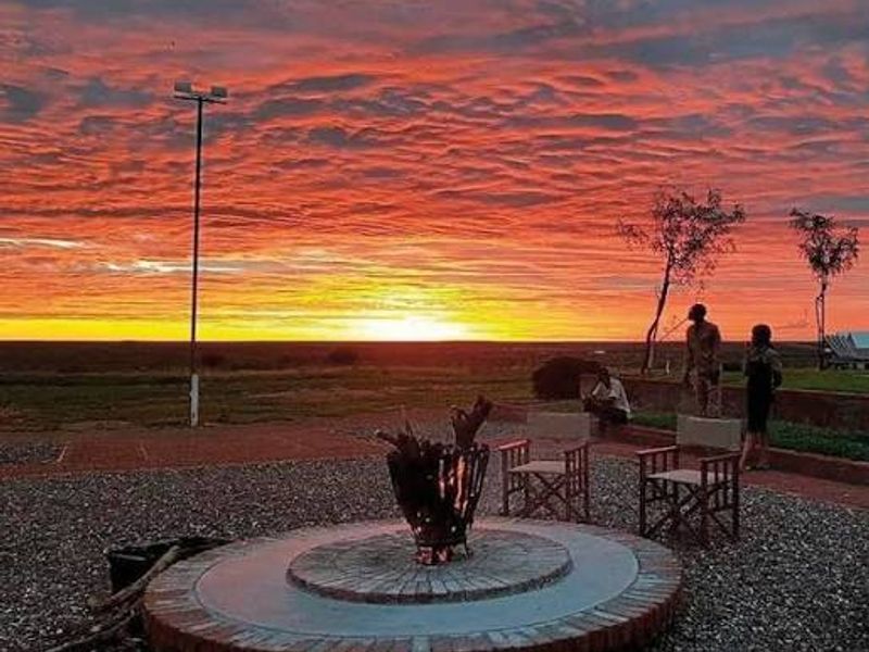 Outdoor entertainment area featuring a circular brick fire pit set within a gravel patio, overlooking a vast landscape at sunset.