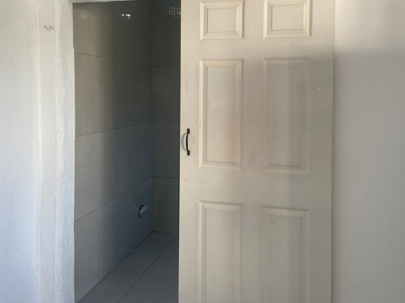 A view into a small, empty bathroom featuring tiled walls and flooring, accessed via a white panel door.
