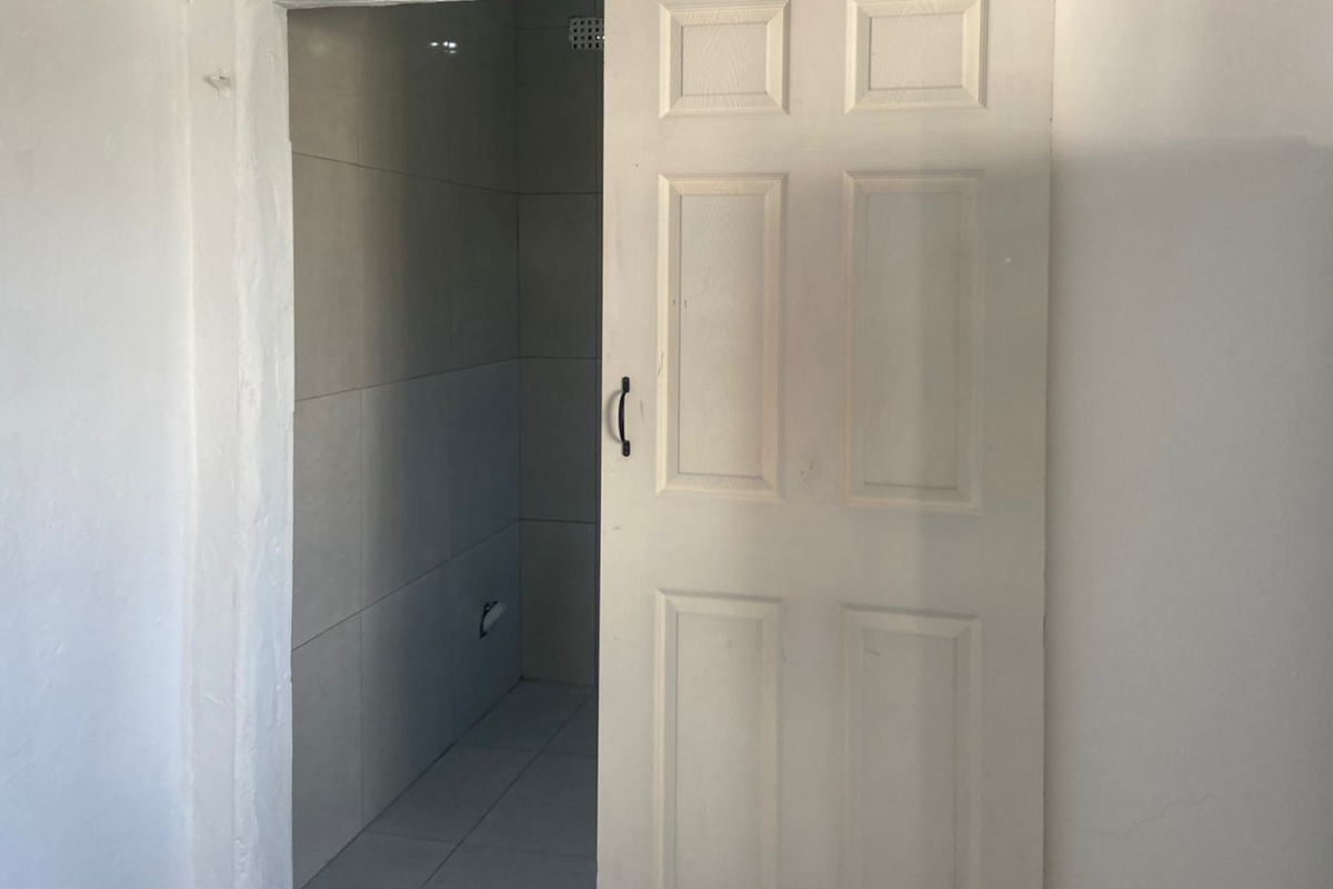 A view into a small, empty bathroom featuring tiled walls and flooring, accessed via a white panel door.