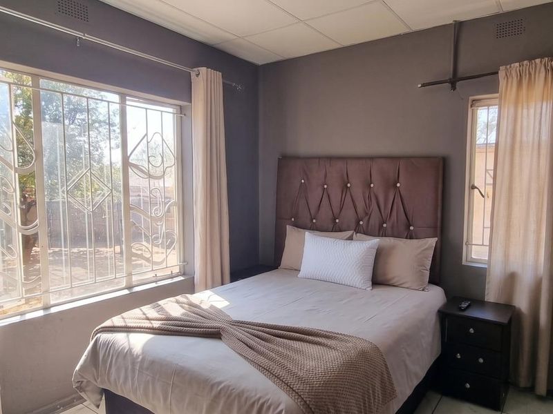 A bedroom featuring tiled flooring, a drop ceiling, and windows fitted with security bars.