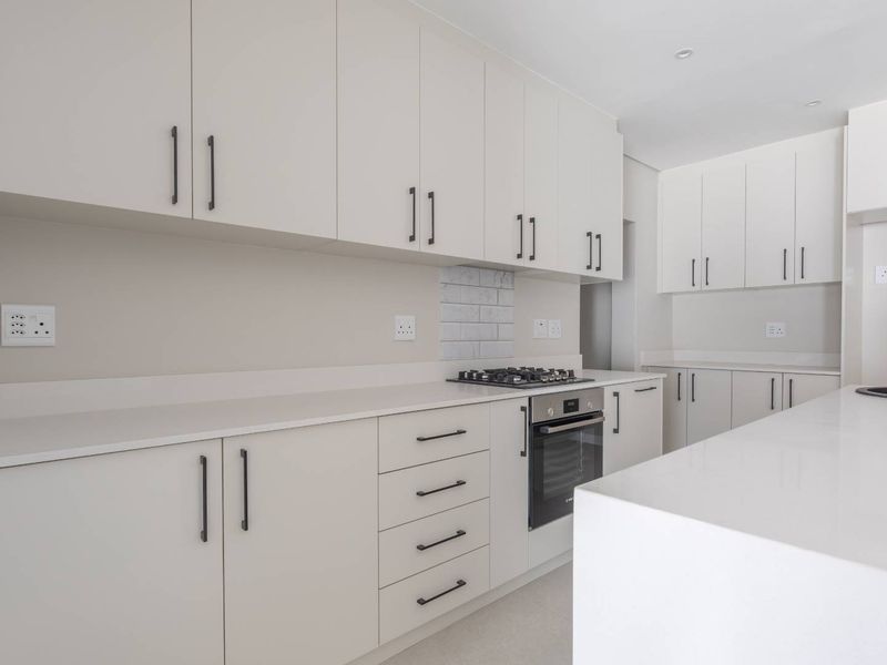 Modern kitchen featuring sleek white cabinetry, stone countertops, a gas hob, built-in oven, and a central island with an undermount sink.