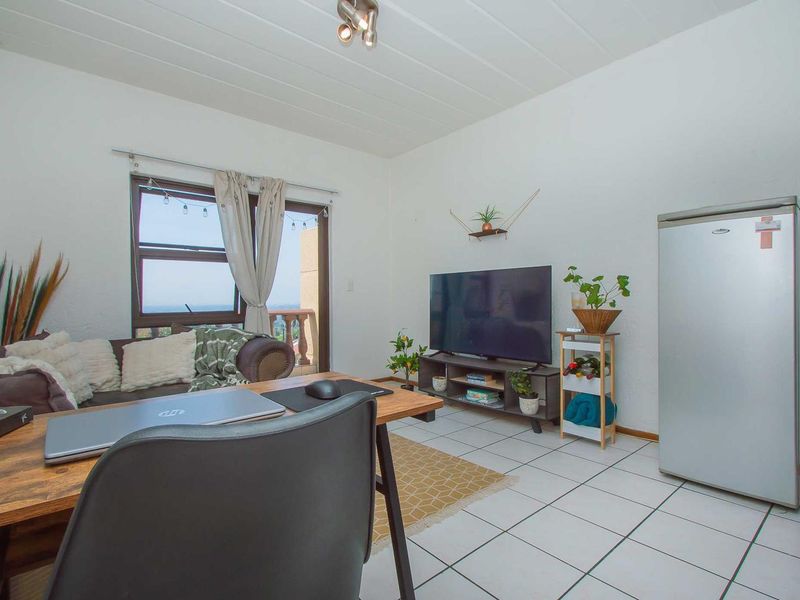 A functional living room featuring tiled flooring, a panelled ceiling, and a sliding glass door providing access to an outdoor balcony area.