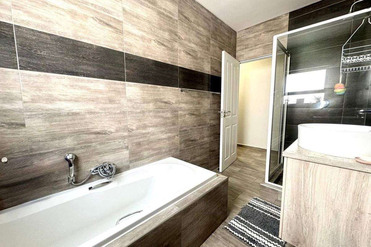 Modern bathroom featuring a built-in bathtub, separate shower enclosure, and a vanity with a vessel sink, finished with contemporary wood-look wall and floor tiles.