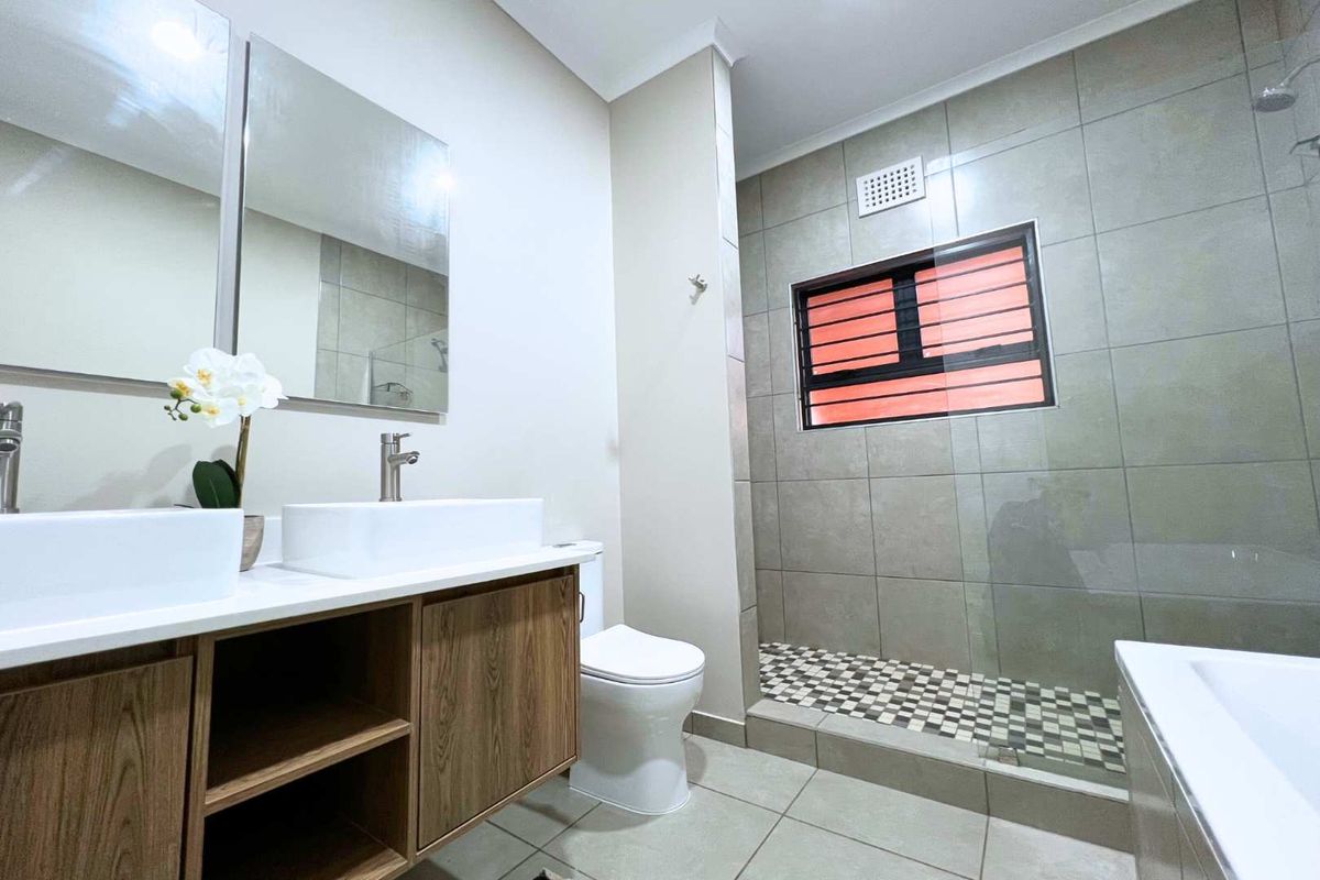Modern bathroom featuring a double vanity with vessel sinks, a walk-in shower with glass enclosure, and neutral floor-to-ceiling tiling.