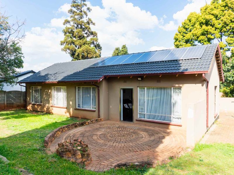 Rear view of the house featuring a circular brick paved patio, large sliding doors, and roof-mounted solar panels set within a garden.