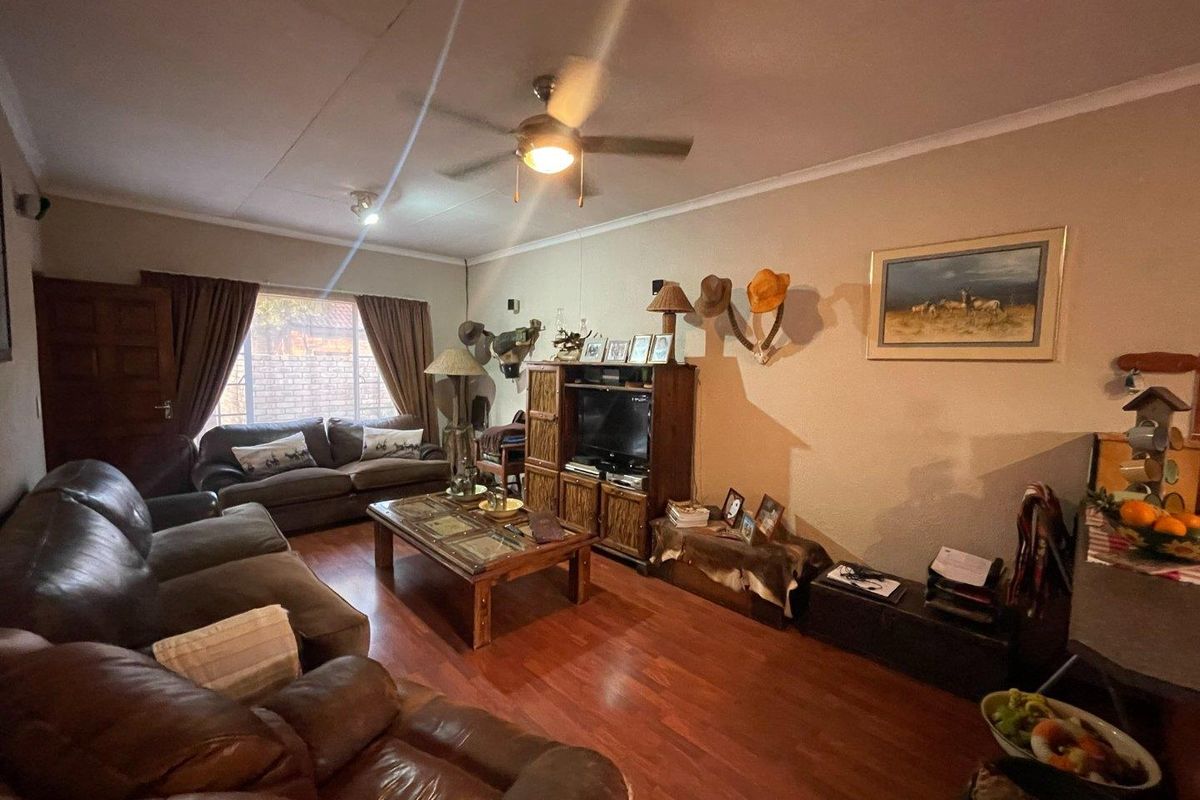 A comfortable living room featuring warm-toned laminate flooring, a ceiling fan, and large windows that provide natural light to the space.