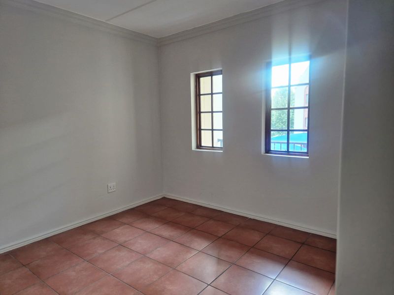 An empty bedroom featuring tiled flooring, neutral walls, and two windows with wooden frames, providing a blank canvas for personalization.