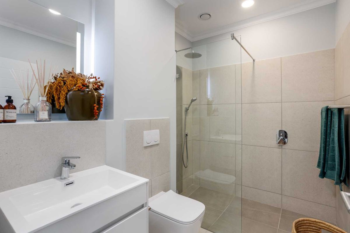Modern bathroom featuring a walk-in glass shower, wall-mounted toilet, and a sleek vanity with integrated basin and mirror.