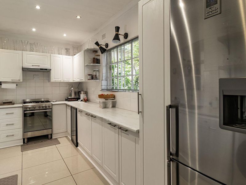 Modern kitchen featuring white cabinetry, stone countertops, stainless steel gas stove, extractor fan, and tiled flooring with recessed lighting.