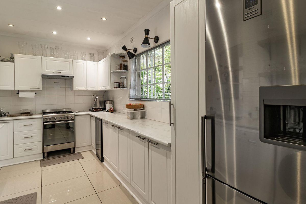 Modern kitchen featuring white cabinetry, stone countertops, stainless steel gas stove, extractor fan, and tiled flooring with recessed lighting.