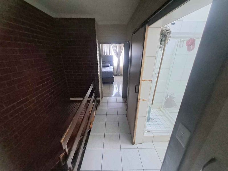 A hallway area featuring tiled flooring and an exposed brick wall, providing access to a bathroom and bedroom.