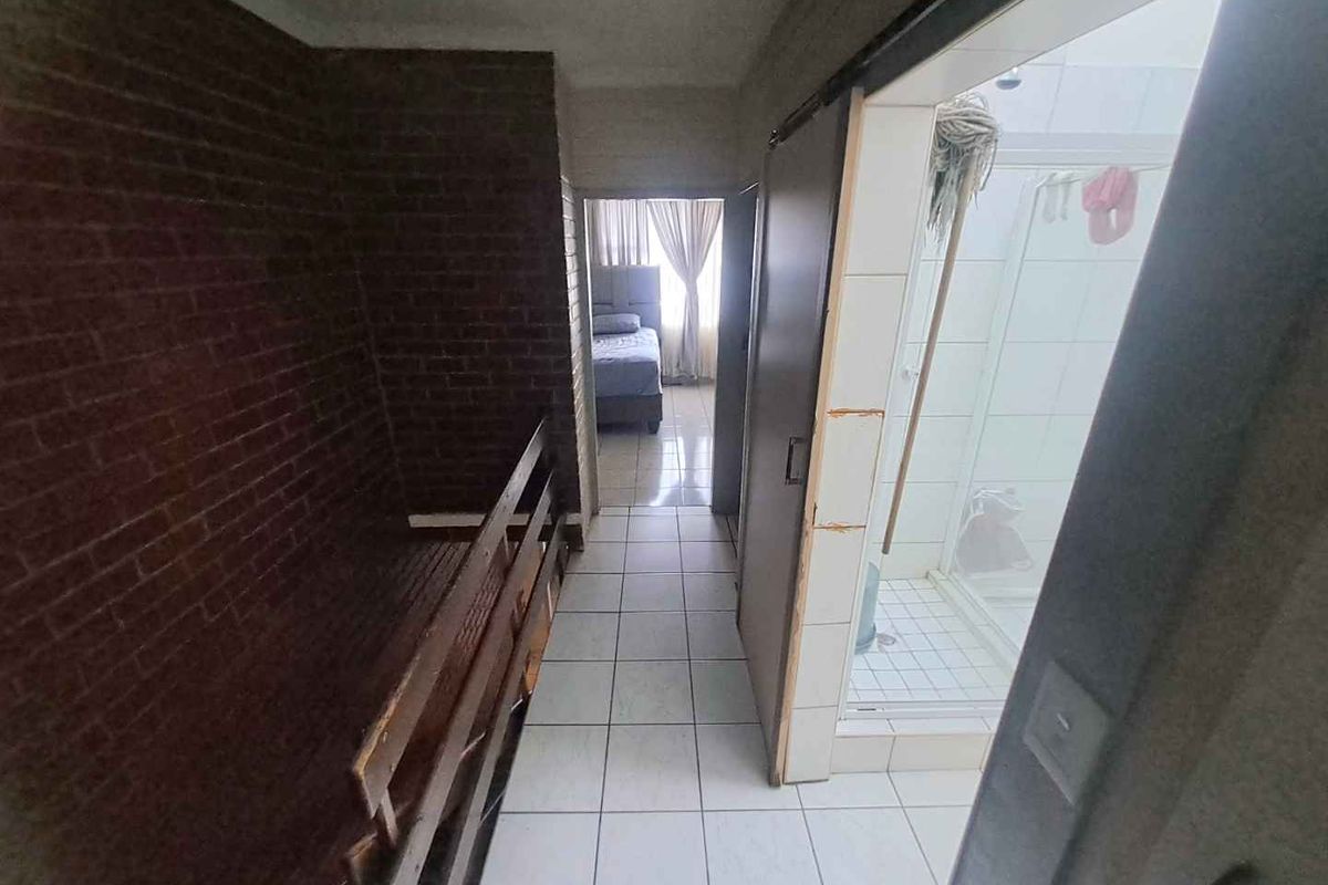 A hallway area featuring tiled flooring and an exposed brick wall, providing access to a bathroom and bedroom.