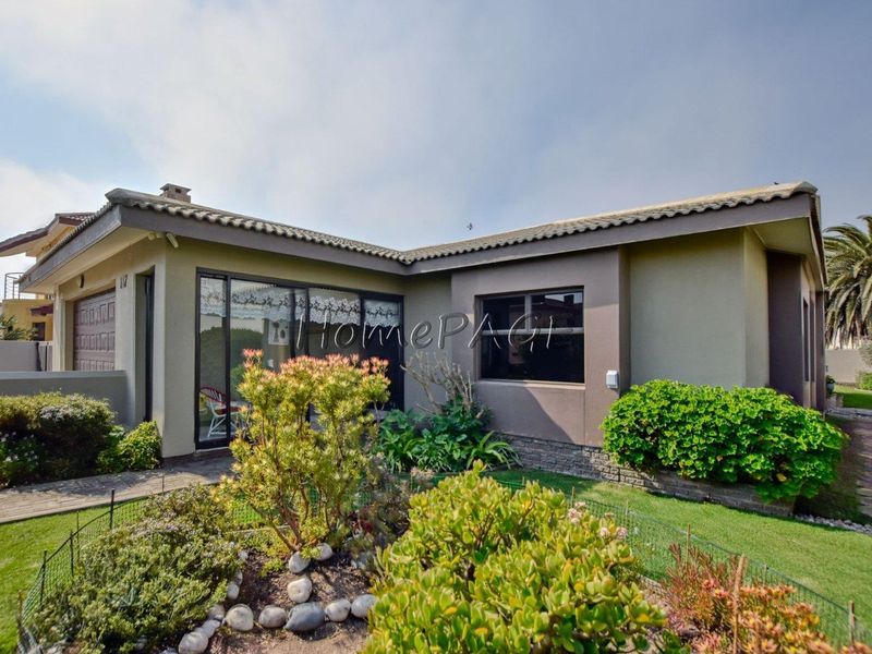 A well-maintained rear exterior view of the house featuring a paved walkway, landscaped garden, stone cladding accents, and sliding glass doors.